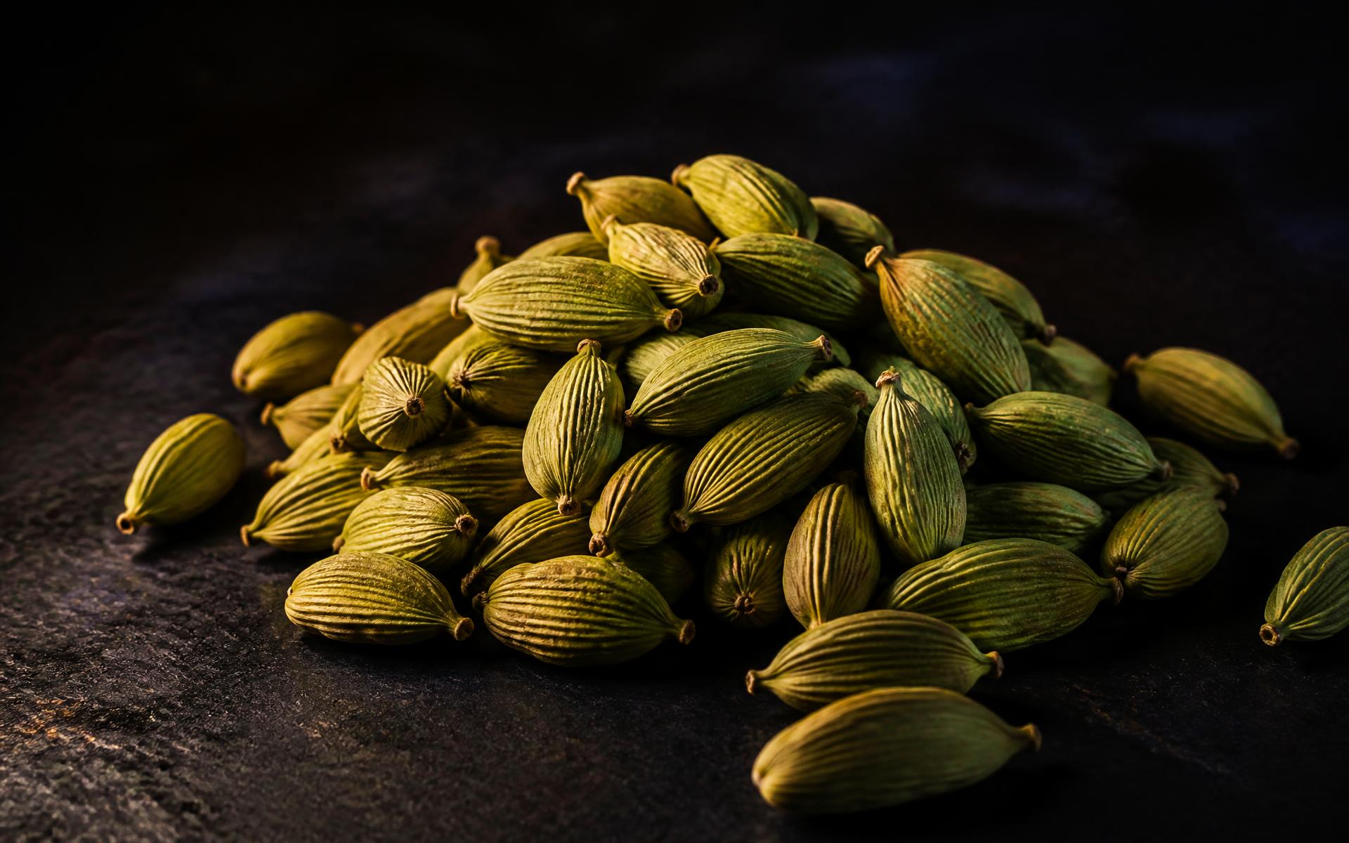 Premium green cardamom pods lit by warm gold light on a dark surface